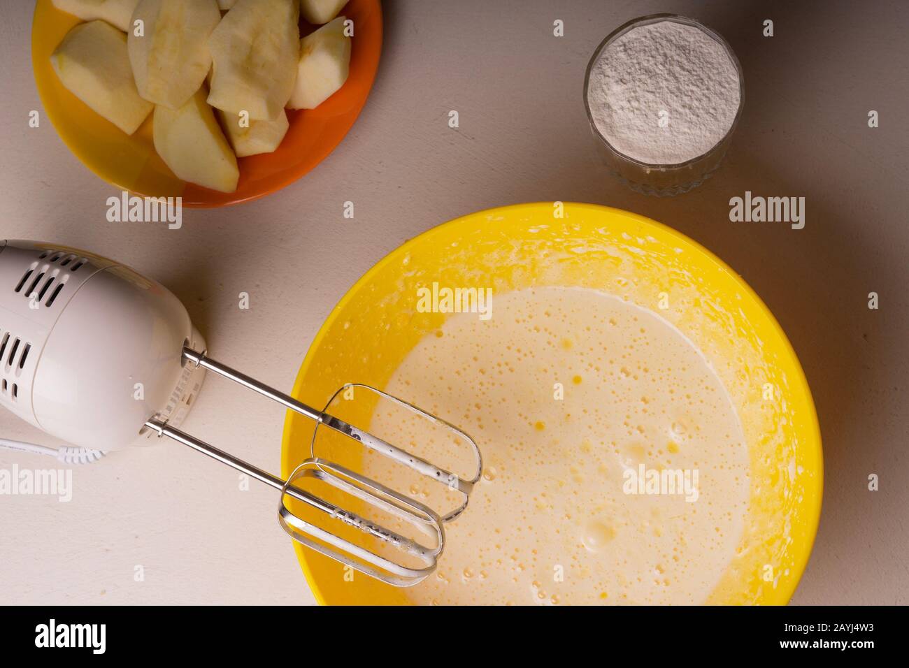 Una donna mescola gli ingredienti per una torta in una ciotola gialla con un miscelatore elettrico Foto Stock