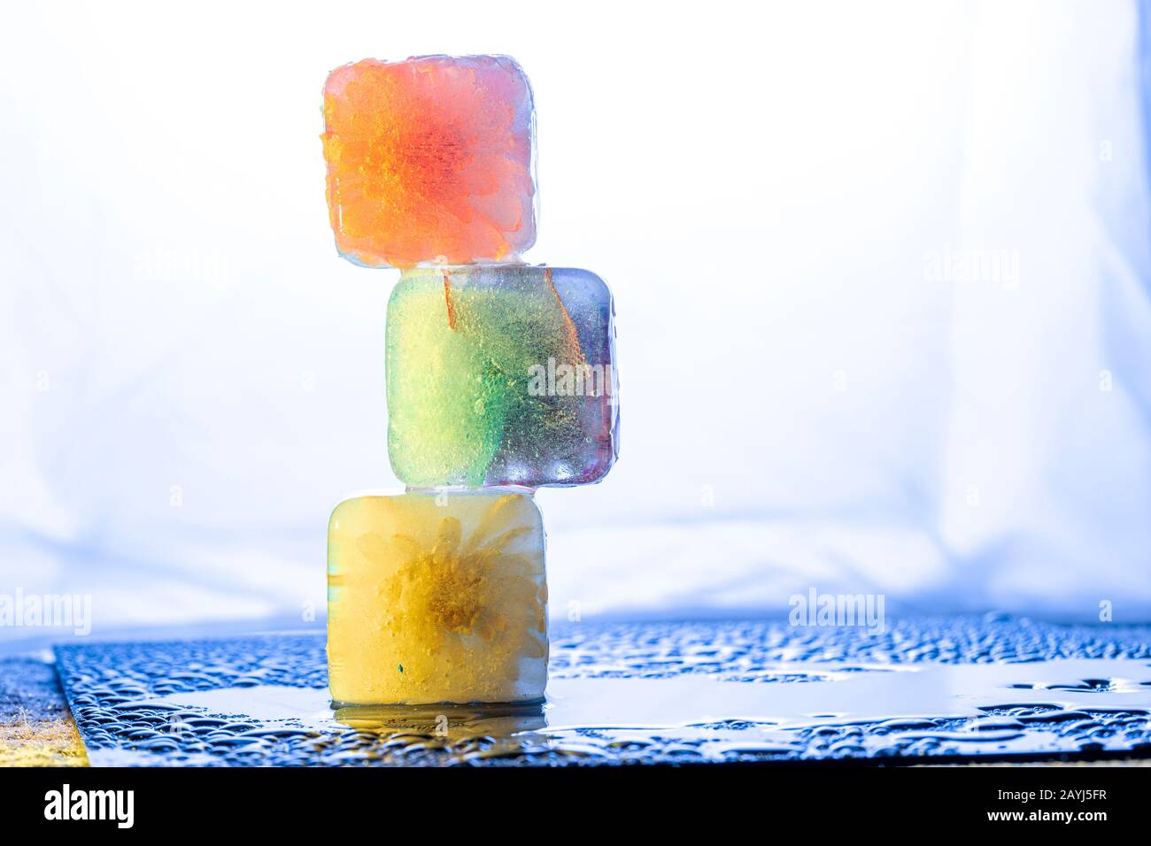 Composizione astratta con cubetti di ghiaccio colorati sovrapposti in tonalità vivaci sul piano del tavolo bagnato Foto Stock