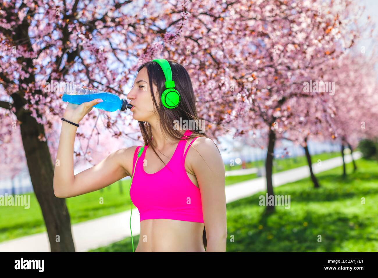 Bevanda energetica femminile durante l'allenamento. Ritratto di donna sportiva bevendo nel parco dopo il jogging. Adatta la musica d'ascolto della ragazza e gioita Foto Stock