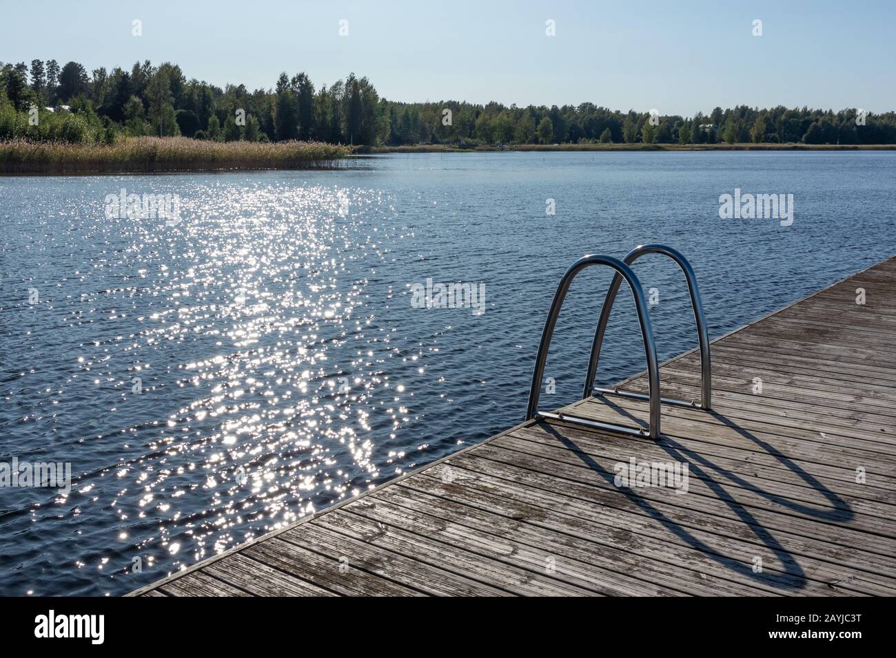 Molo in legno per il nuoto con scala in metallo sul tranquillo lago blu giornata di sole sulla natura Finlandia idilliaca località naturale Foto Stock