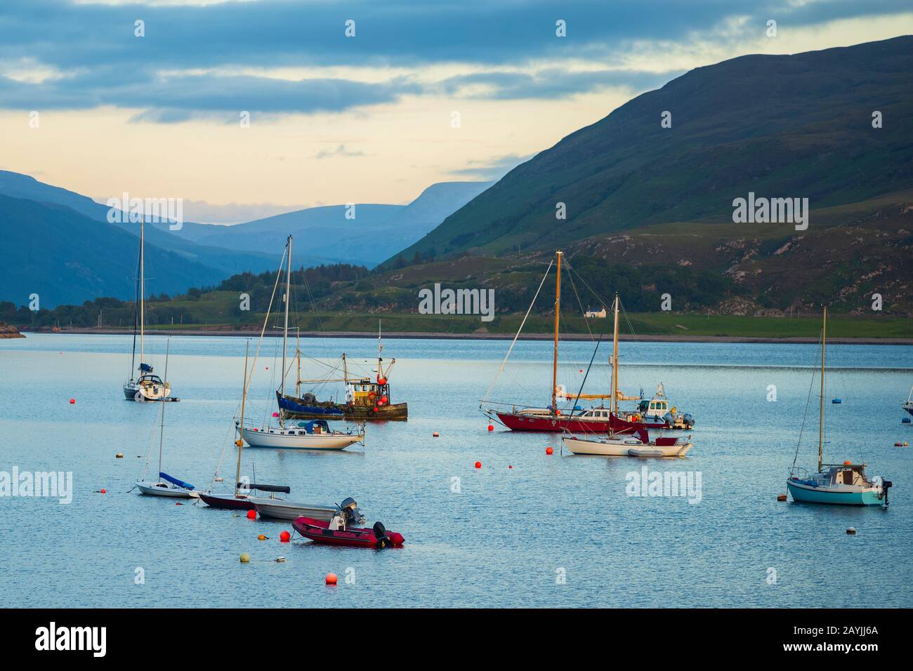 Le barche che sono ancorate in Loch Broom al largo del porto di Ullapool, Scozia, brillano alla luce da un tramonto. Foto Stock