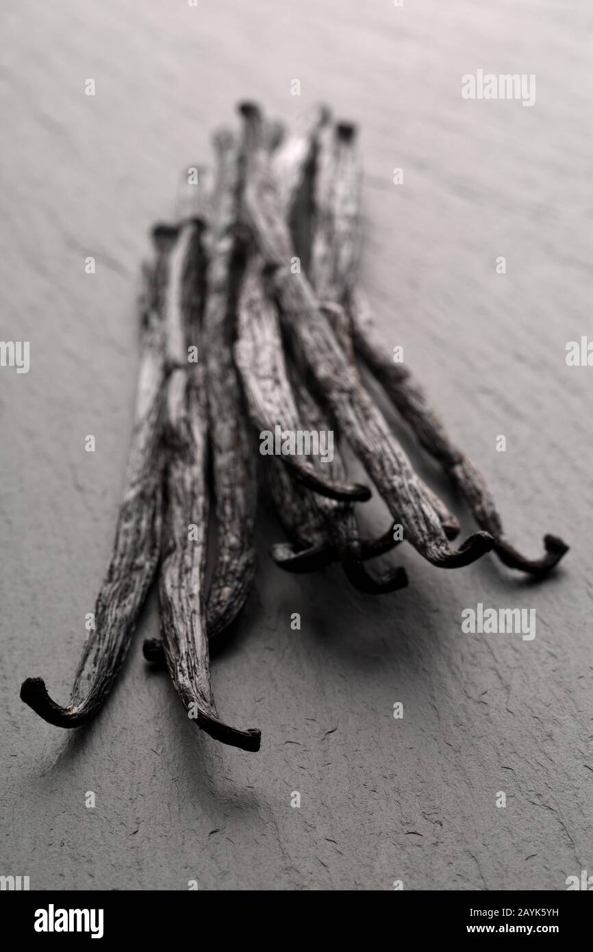 Fascio di baccelli o fagioli di vaniglia borbonici secchi su tavole di pietra nera con messa a fuoco selettiva Foto Stock