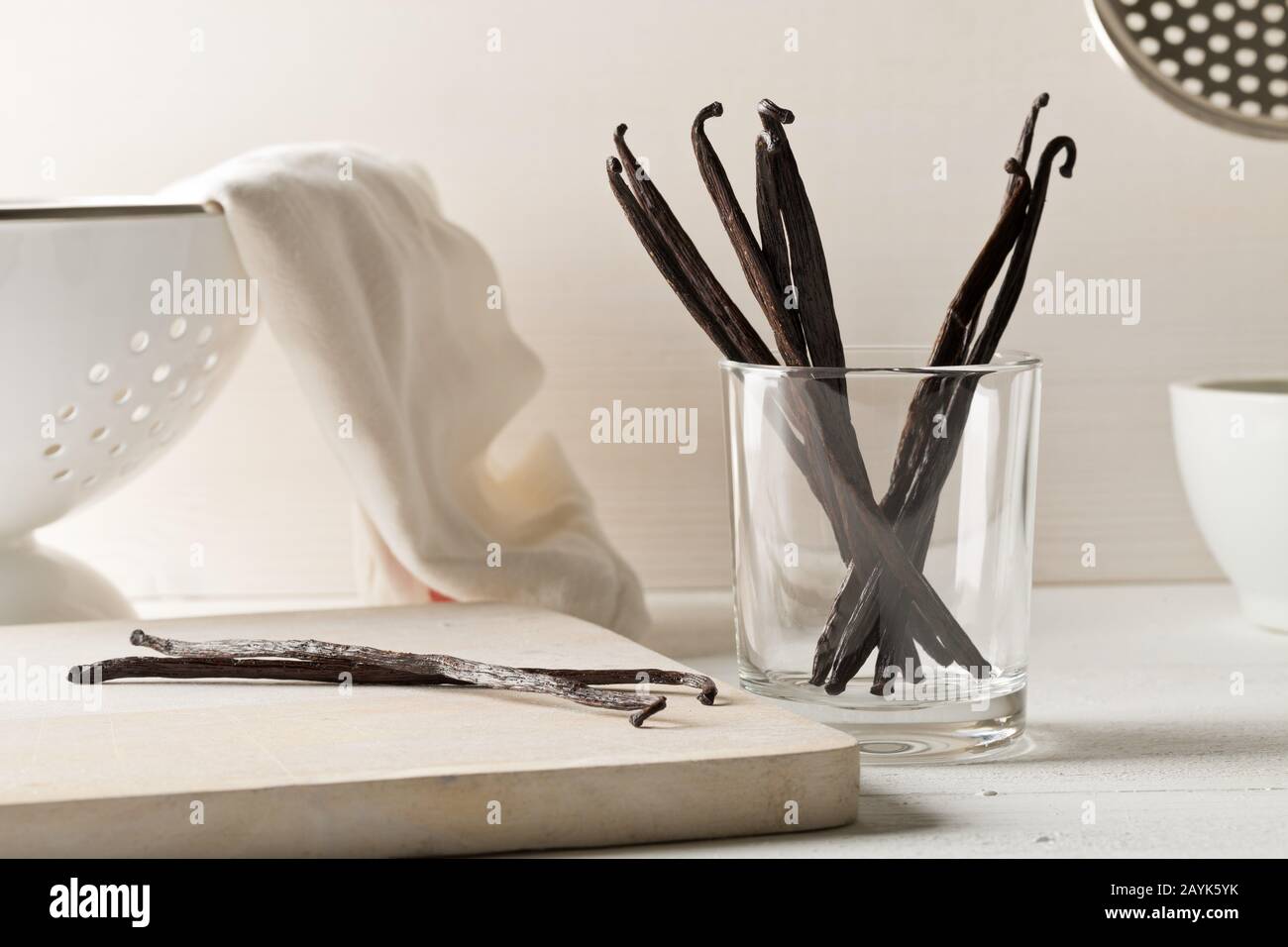 Fascio di baccelli o fagioli di vaniglia bourbon essiccati su tagliere di legno e in vetro su sfondo bianco cucina - fuoco selettivo Foto Stock