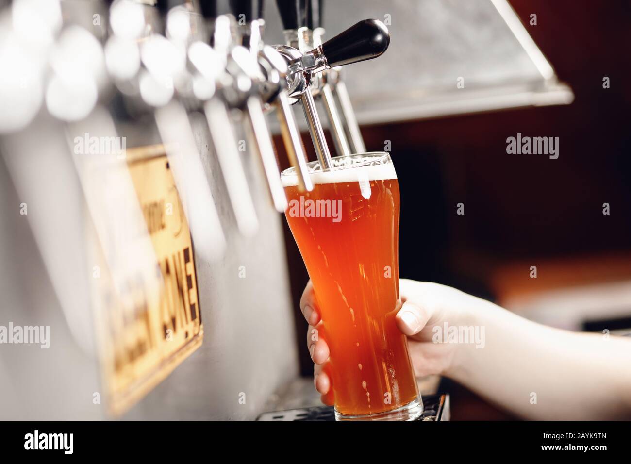 Il getto di birra fresca e leggera viene versato in un calice di vetro su sfondo scuro con spruzzi e schiuma Foto Stock