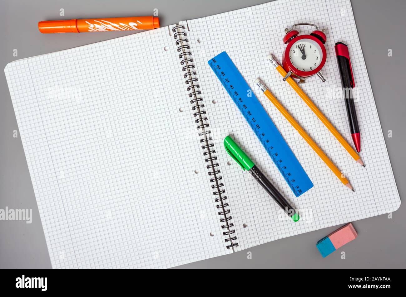 Matite, una penna e un righello si trovano su un notebook aperto. Una sveglia ricorda l'ora. Ufficio. Forniture scolastiche. Foto Stock