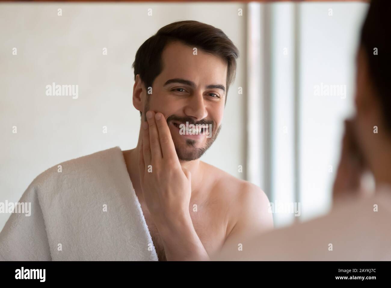 Sorridente uomo millenario applicare la lozione per il viso dopo la rasatura Foto Stock