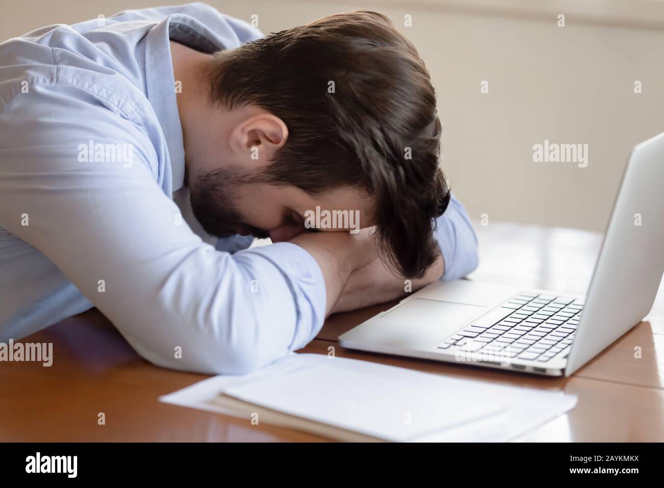 Un giovane stanco si addormenta vicino al laptop sul posto di lavoro Foto Stock