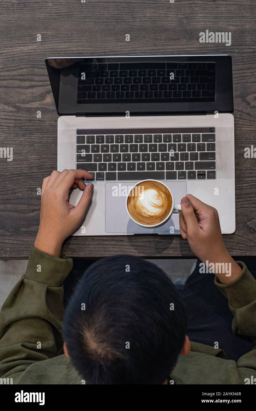 Uomo che beve caffè caldo e che usa un computer portatile Foto Stock