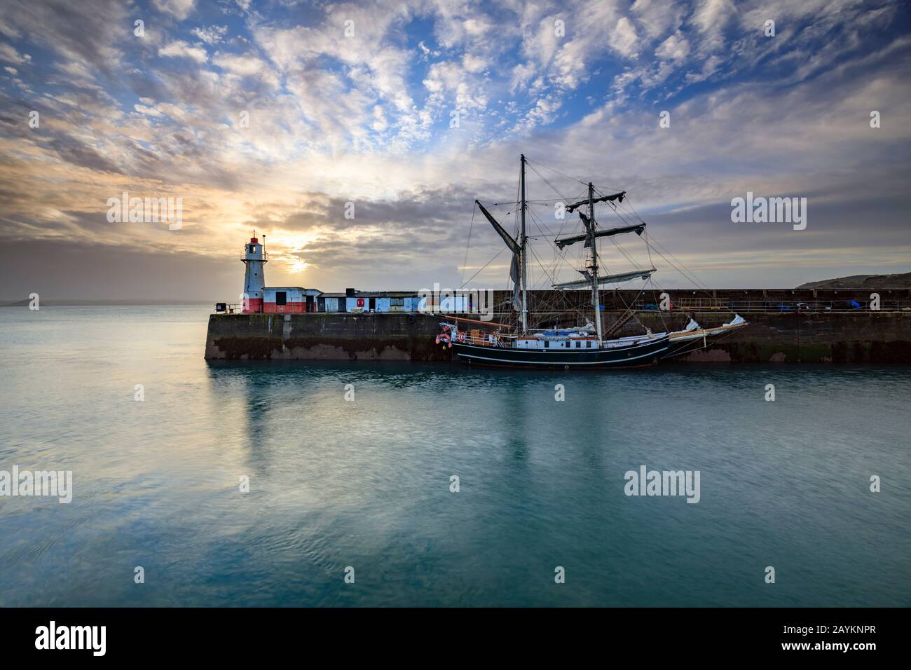 Una nave alta e il faro alla bocca del Porto di Newlyn catturati all'alba Foto Stock