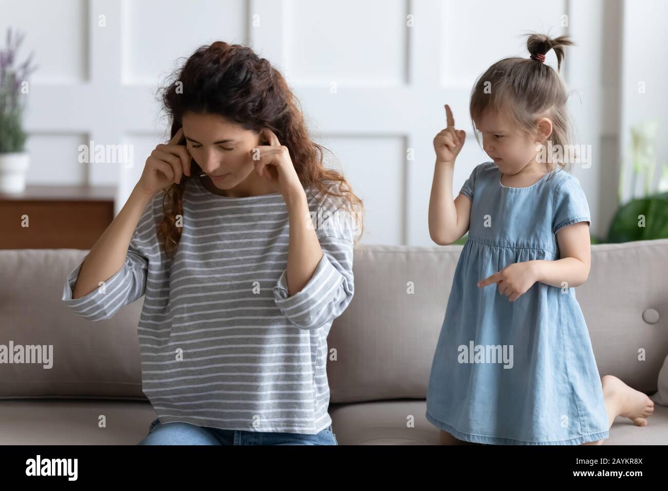 Giovane madre stressata che copre le orecchie, infastidita dal cattivo comportamento delle figlie. Foto Stock