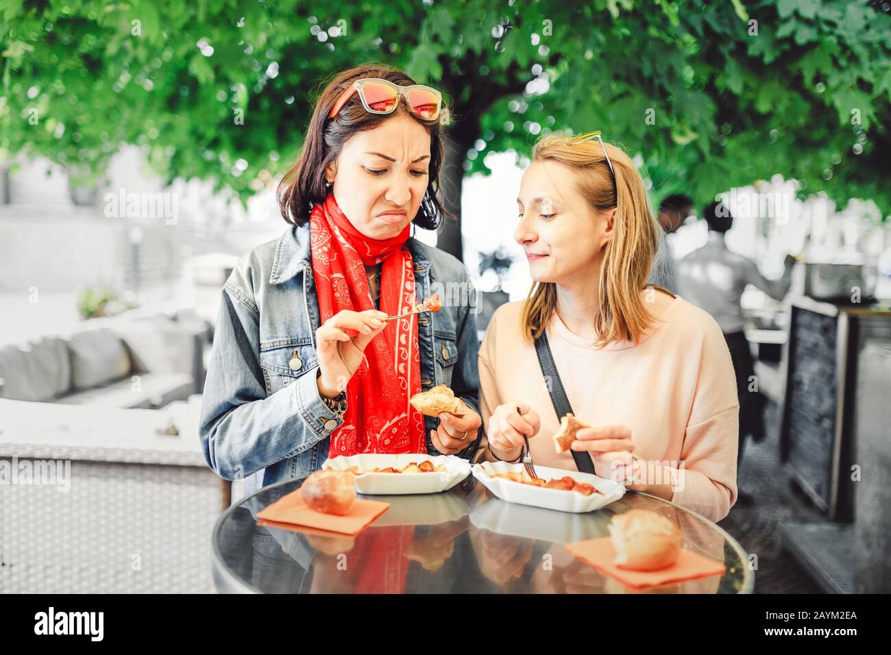 Due ragazze amici studenti cercando salsiccia con impasse di disgusto sul loro volto. Il concetto di fast food viziato Foto Stock