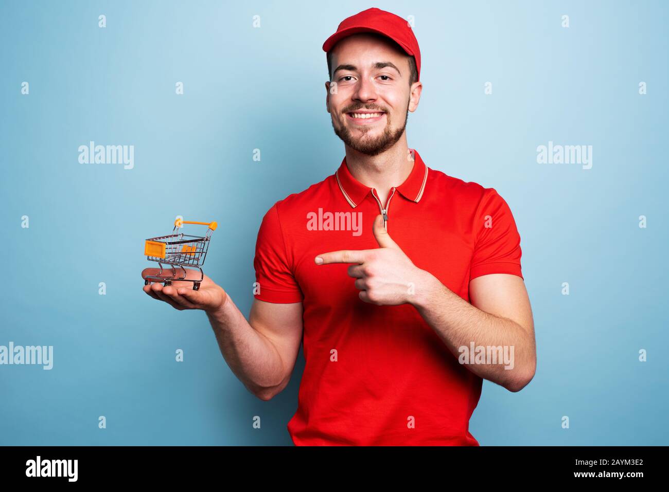 Corriere uomo mostra il carrello dove acquistare. Sfondo ciano Foto Stock