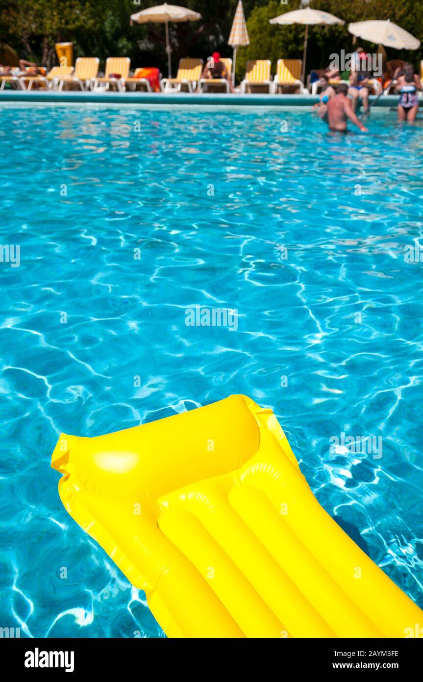 Luminoso lilo giallo che galleggia al sole su una piscina blu ondulata Foto Stock