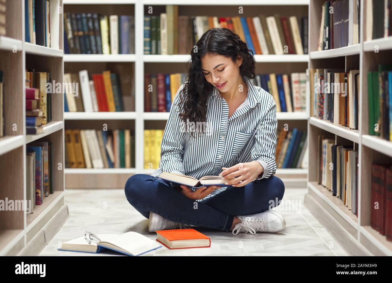 Sorridente latina ragazza leggere libri in biblioteca Foto Stock