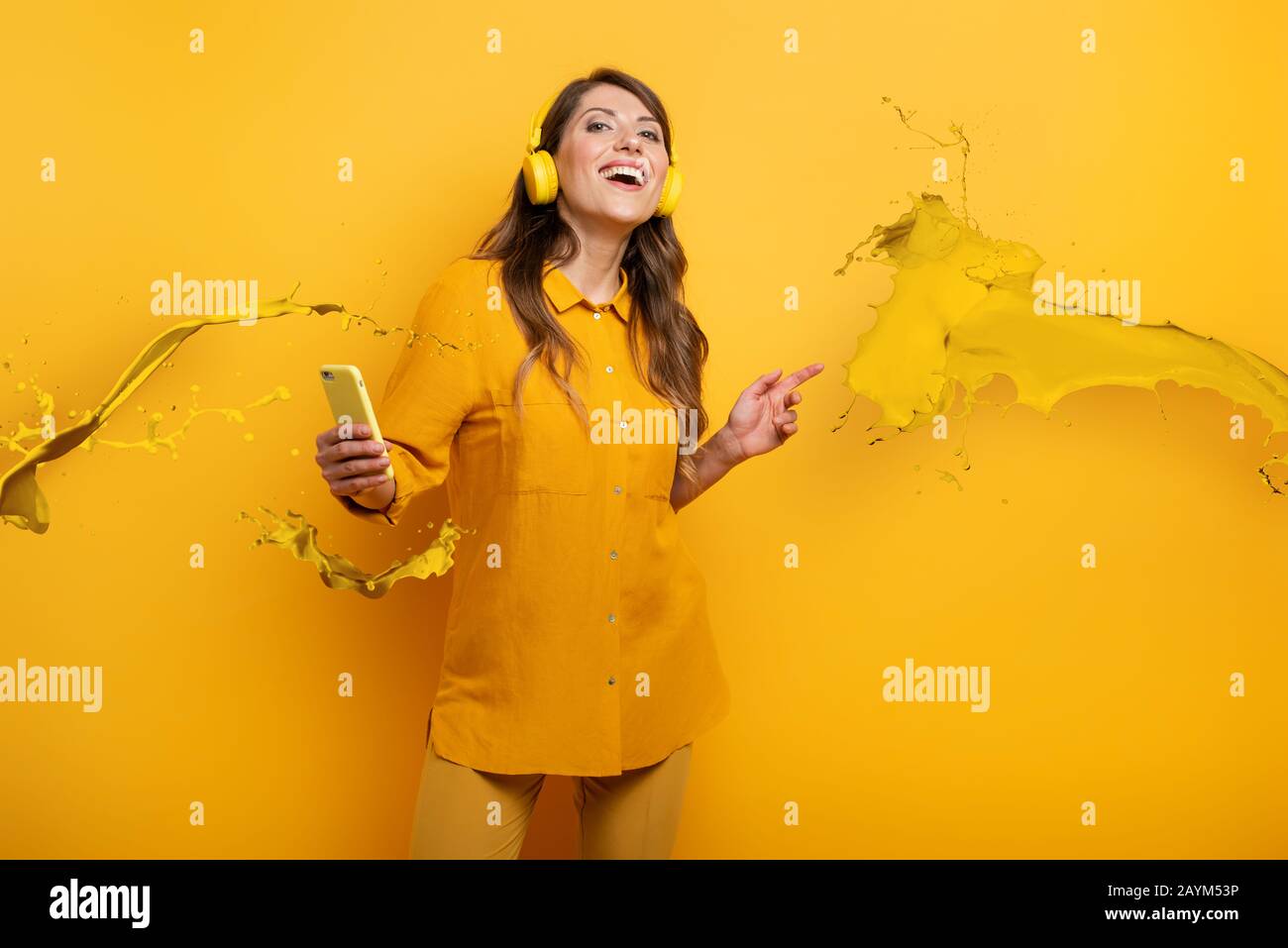 Ragazza con auricolare giallo ascolta musica e danze. emozionale e espressione energica Foto Stock