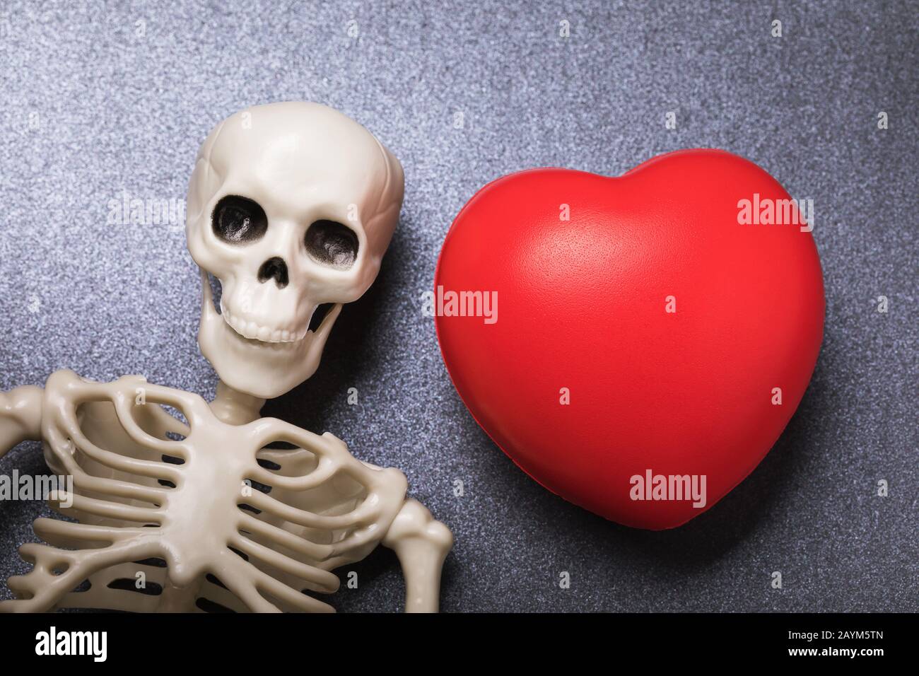 Scheletro e cuore sul tavolo, vista dall'alto. Il concetto di 'amore alla tomba' Foto Stock