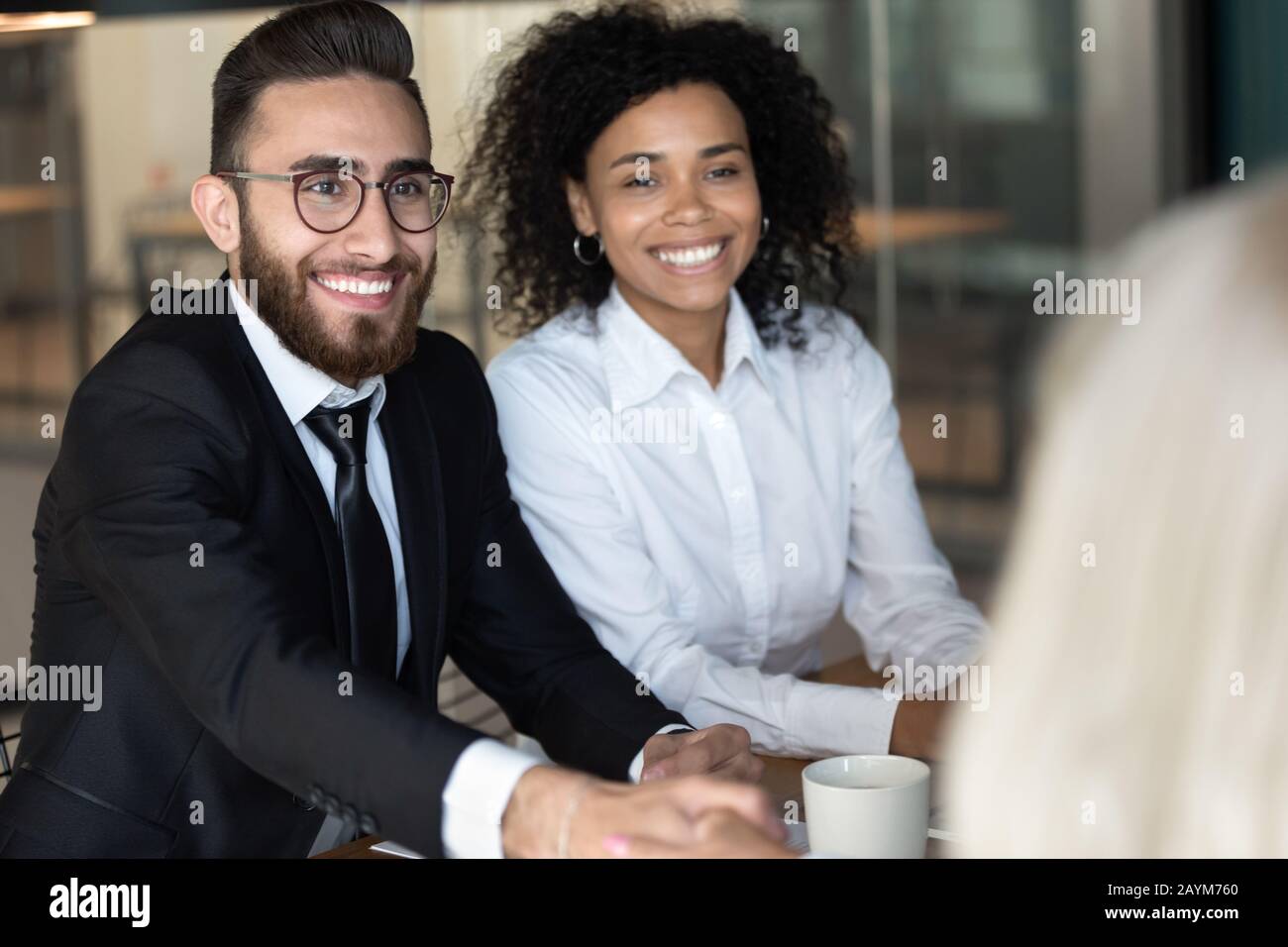 Uomo d'affari arabo che saluta il partner scuotendo le mani seduti alla scrivania Foto Stock