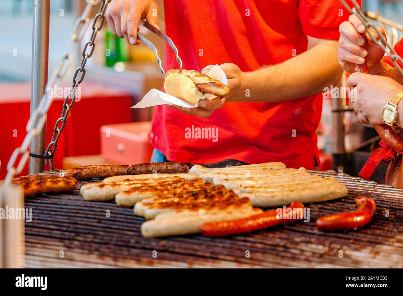 Uomo che cucina le salsicce su un grill piatto al mercato alimentare Street Foto Stock