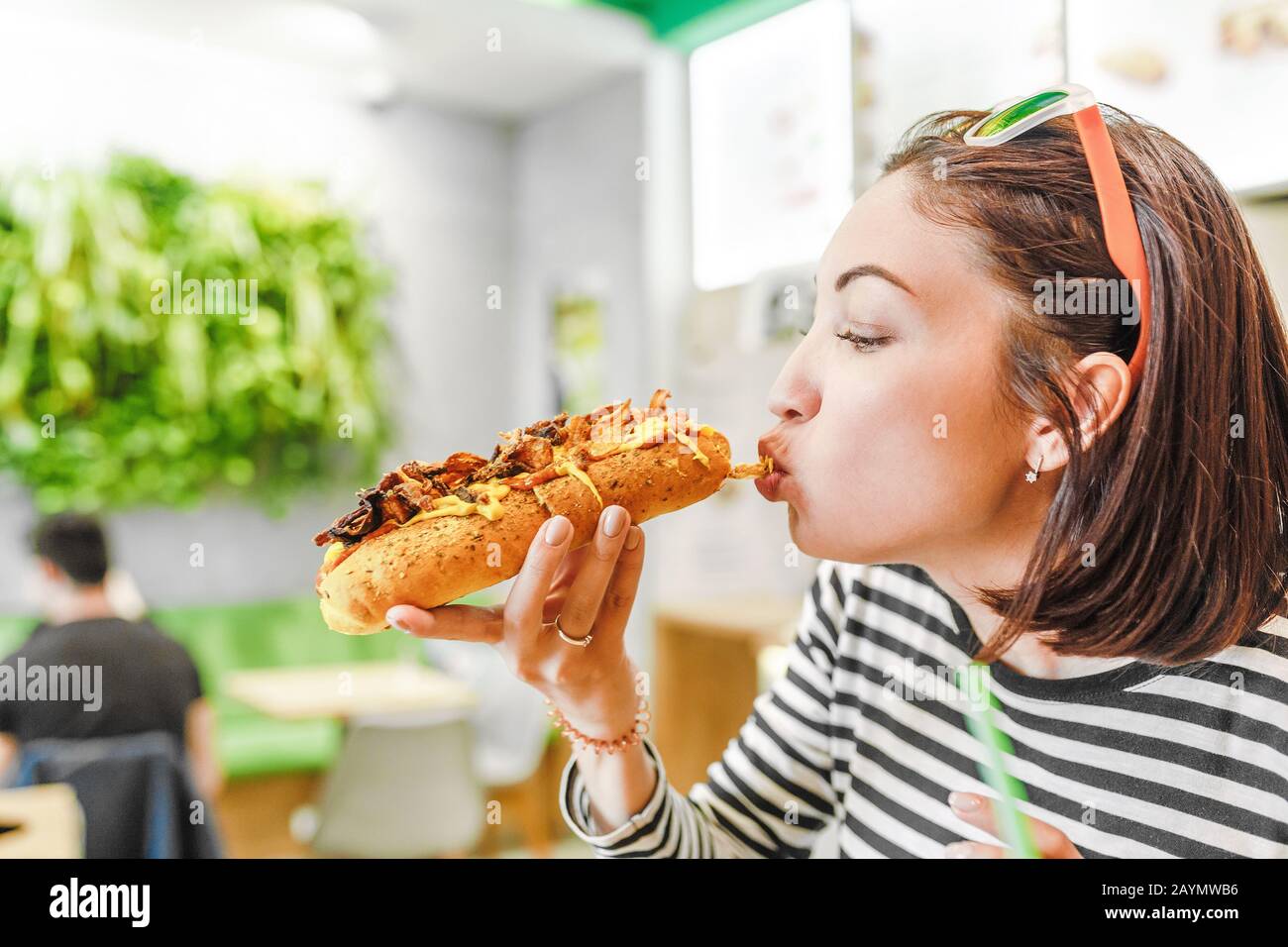 Giovane bella ragazza mangiare hot dog grande in fast food ristorante Foto Stock