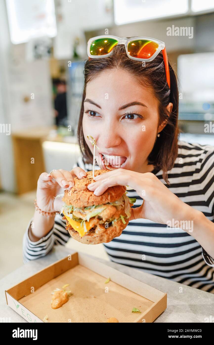 Donna che mangia un hamburger in un moderno fast food, concetto di pranzo Foto Stock
