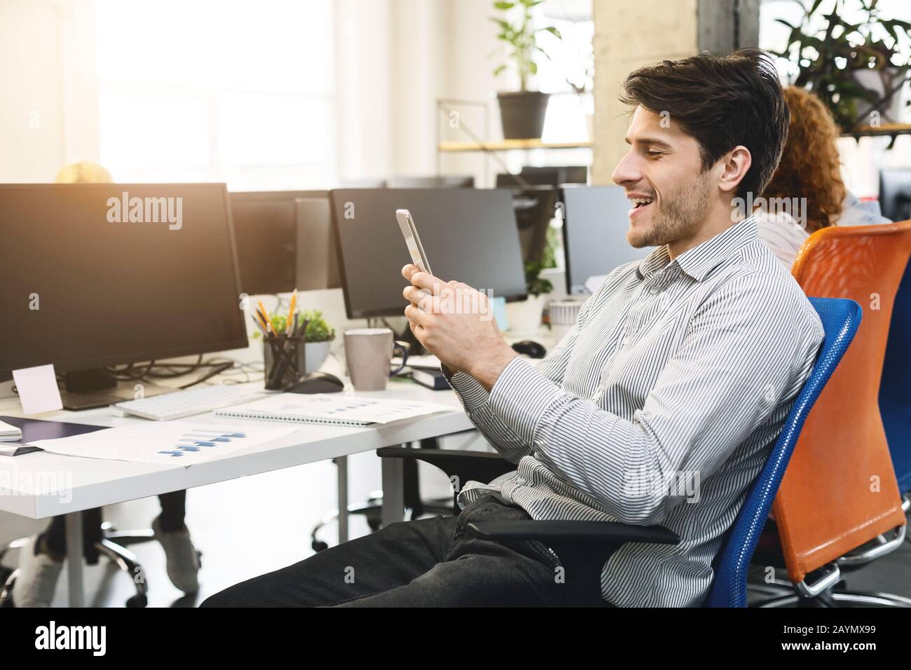 Ragazzo entusiasta che guarda lo schermo del telefono cellulare, gli interni dell'ufficio Foto Stock