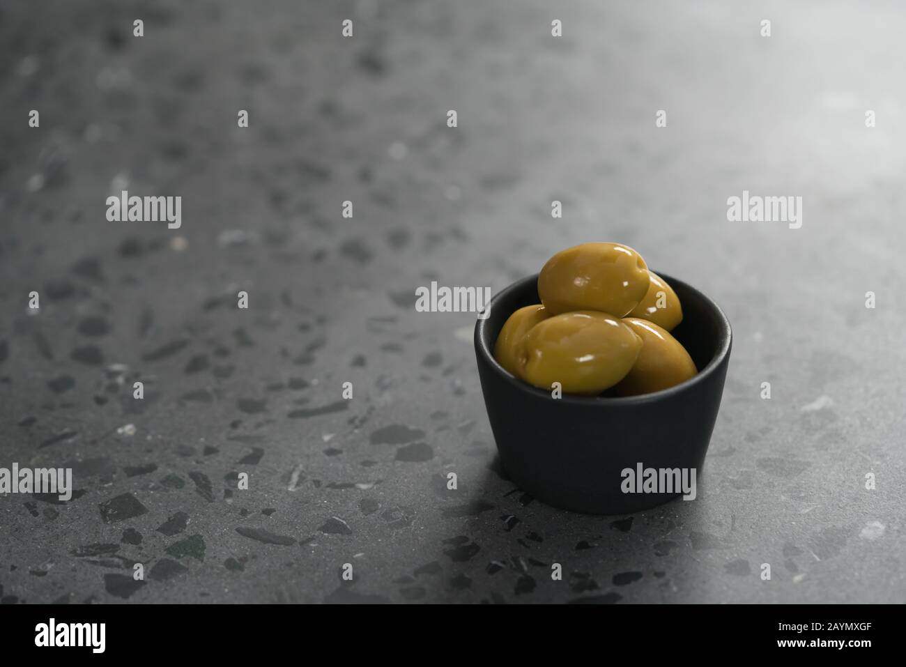 Olive verdi intere in una piccola ciotola nera su fondo in cemento, fuoco poco profondo Foto Stock