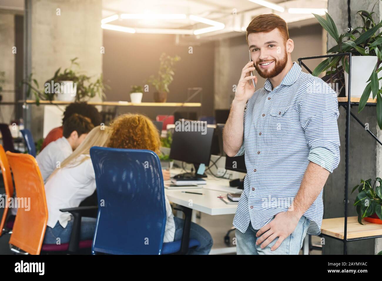Giovane ragazzo allegro che parla per telefono durante l'orario di lavoro Foto Stock