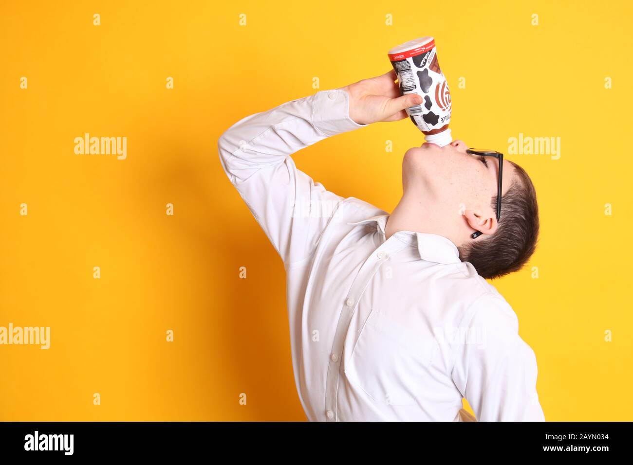 Un giovane ragazzo di età 8yrs beve una bottiglia di cioccolato Muller Frijj su sfondo giallo Foto Stock