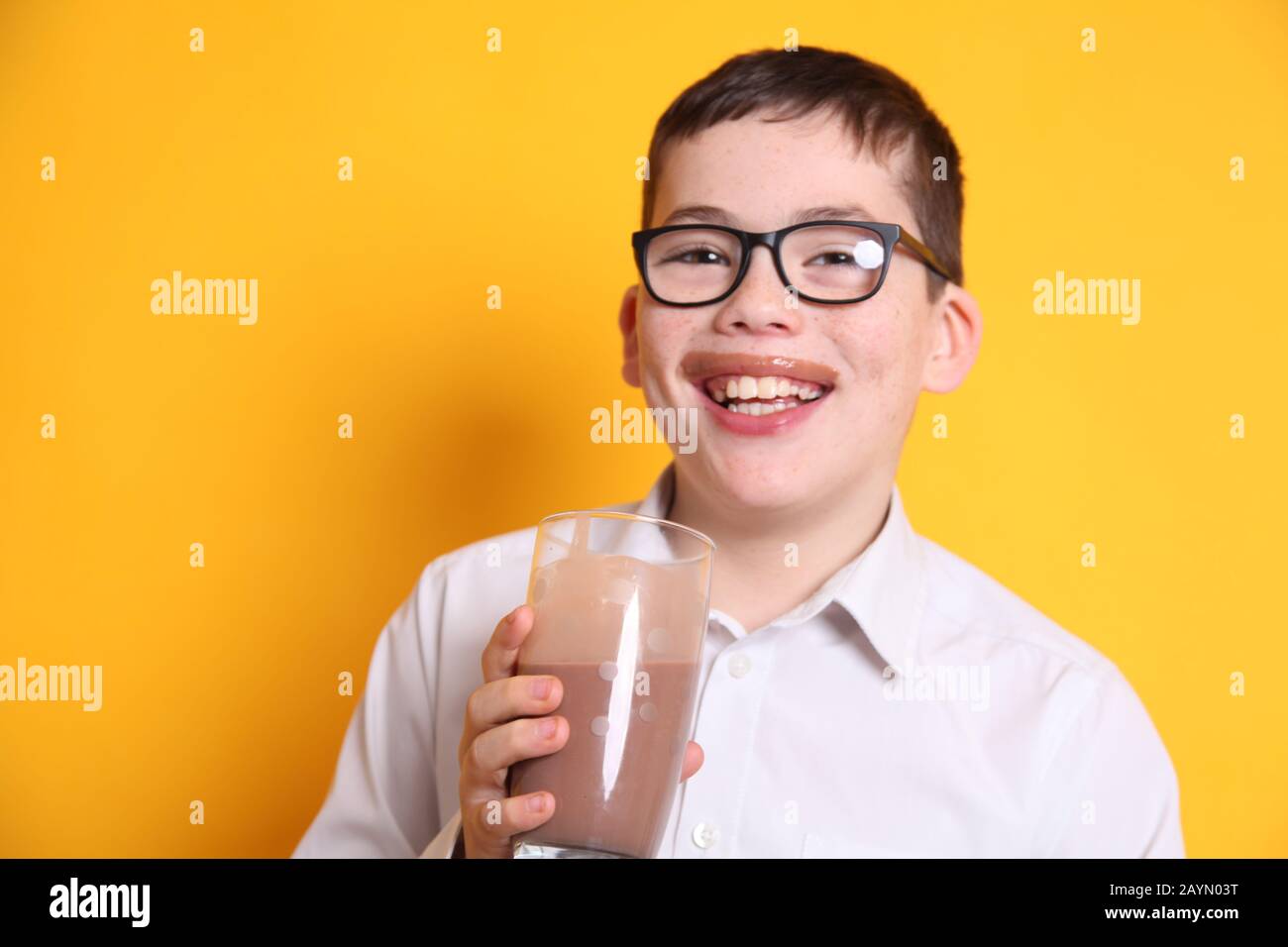 Un giovane ragazzo di 8yrs vecchio beve un bicchiere di latte al cioccolato con labbro superiore ricoperto di cioccolato su sfondo giallo Foto Stock