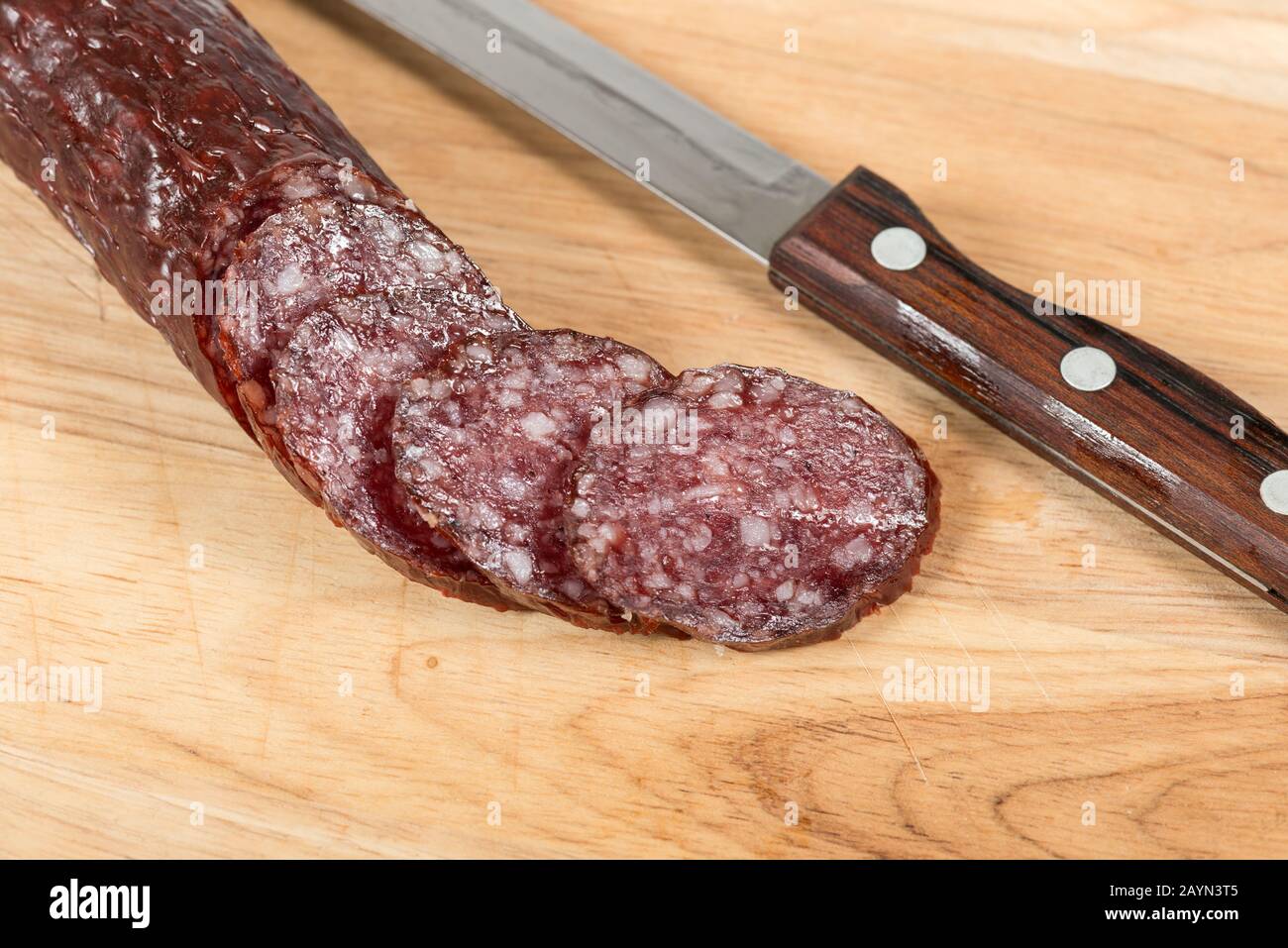 Salame asciutto all'aria, bastoncino e coltello su tavola di legno con fette. Primo piano. Vista dall'alto Foto Stock