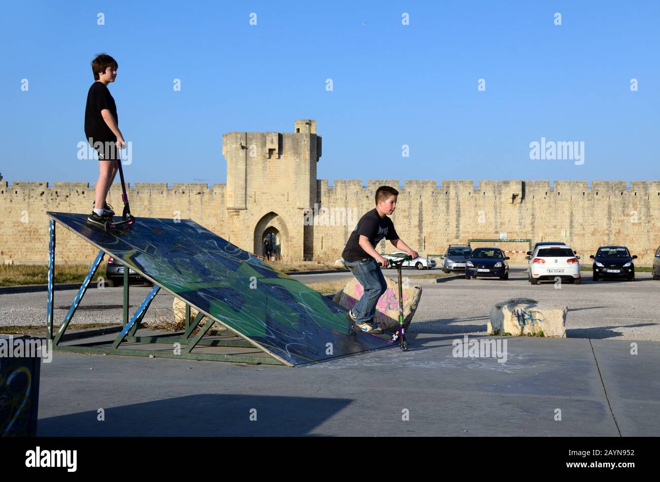 Ragazzi in Skatepark giocando su Scooters, Push-Scooters o Kick Scooters di fronte Ai Bastioni medievali della città Murata di Aigues-Mortes Camargue Francia Foto Stock