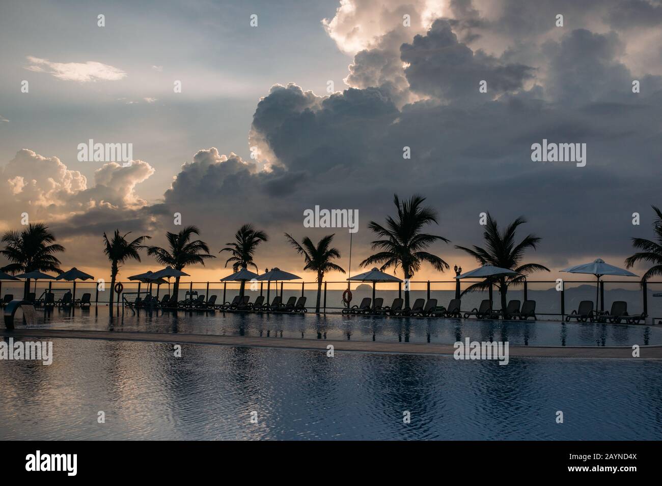 Piscina, palme intorno, riflessione di palme in piscina, alba con un bel cielo nuvoloso. Un'area vuota con molti lettini, il pas del sole Foto Stock