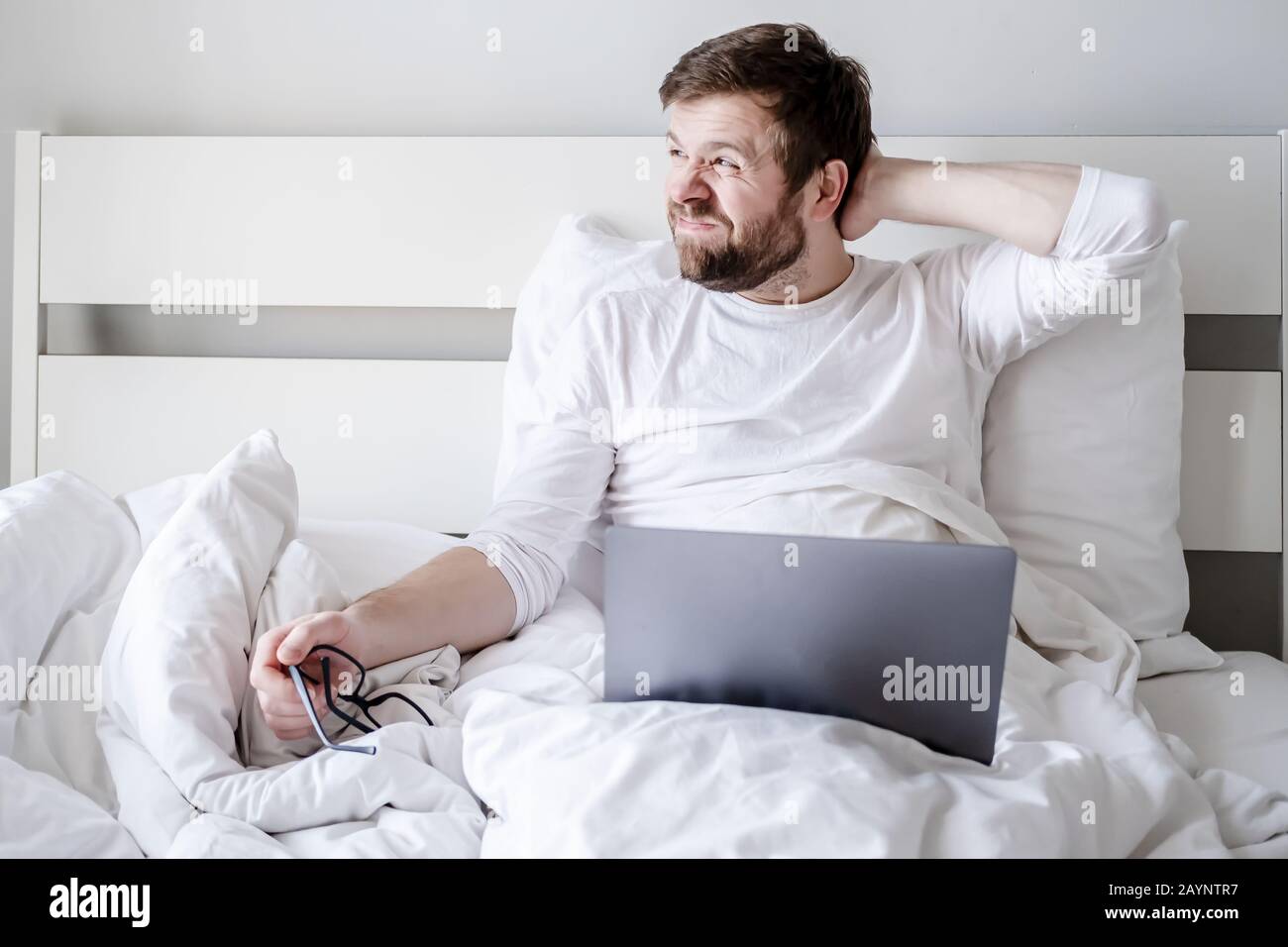 Processo creativo. Blogger distratto dal lavorare con un computer portatile, ha tolto gli occhiali e guarda attentamente fuori la finestra a letto. Foto Stock