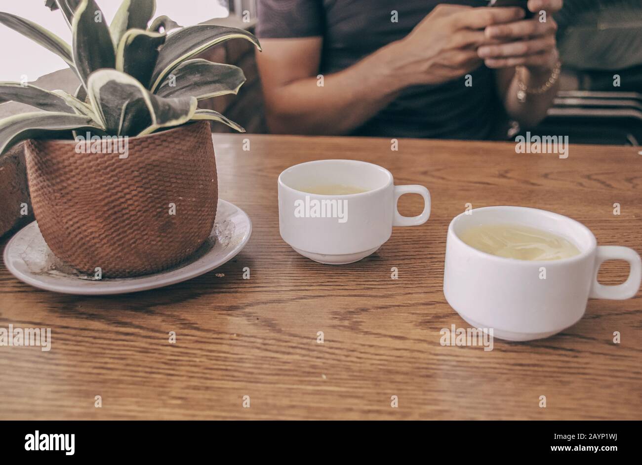 Foto concettuale che mostra due tazze di tè e una persona che utilizza il telefono per mostrare gli effetti della tecnologia, dei social media e di Internet nella lif quotidiana Foto Stock