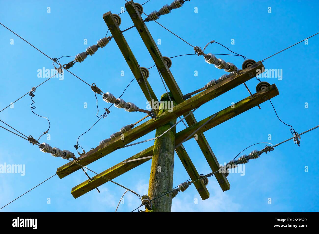Vista ravvicinata di un palo da lavoro in legno con cavi di alimentazione e isolatori a soffitto contro un cielo blu. Foto Stock