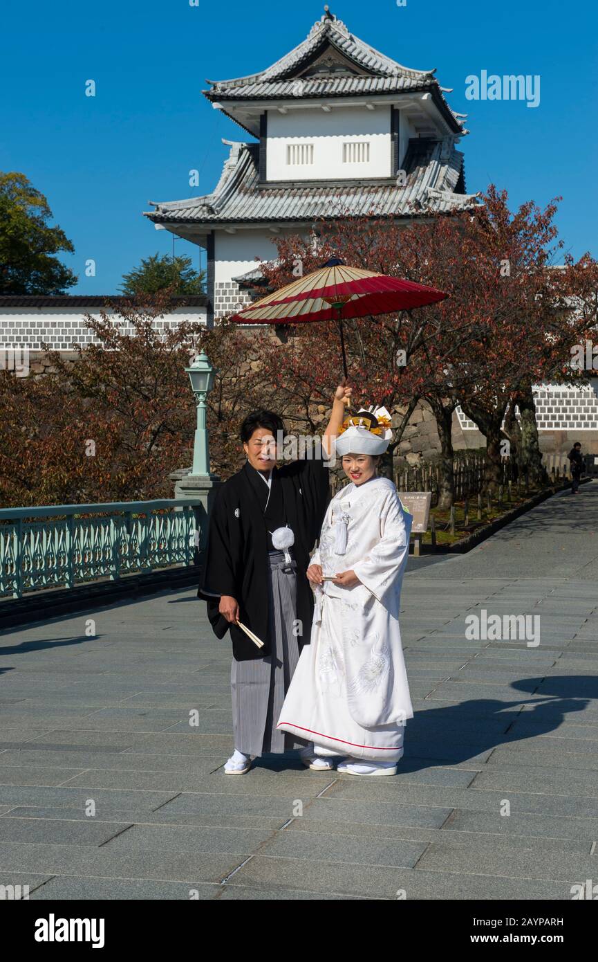 Una coppia di matrimoni in abiti tradizionali si trova di fronte al castello nel Parco del Castello di Kanazawa a Kanazawa, nella prefettura di Ishikawa, sull'Isola di Honshu Foto Stock