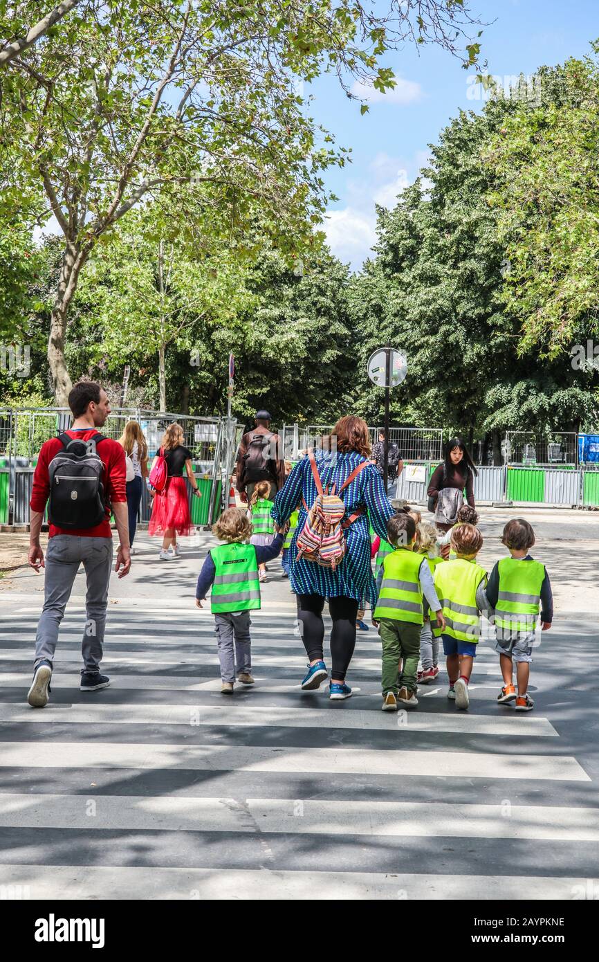 Bambini della scuola giovane in giacche ad alta visibilità che sono scortati dagli adulti attraverso un incrocio di zebra a Parigi, Francia, Europa Foto Stock