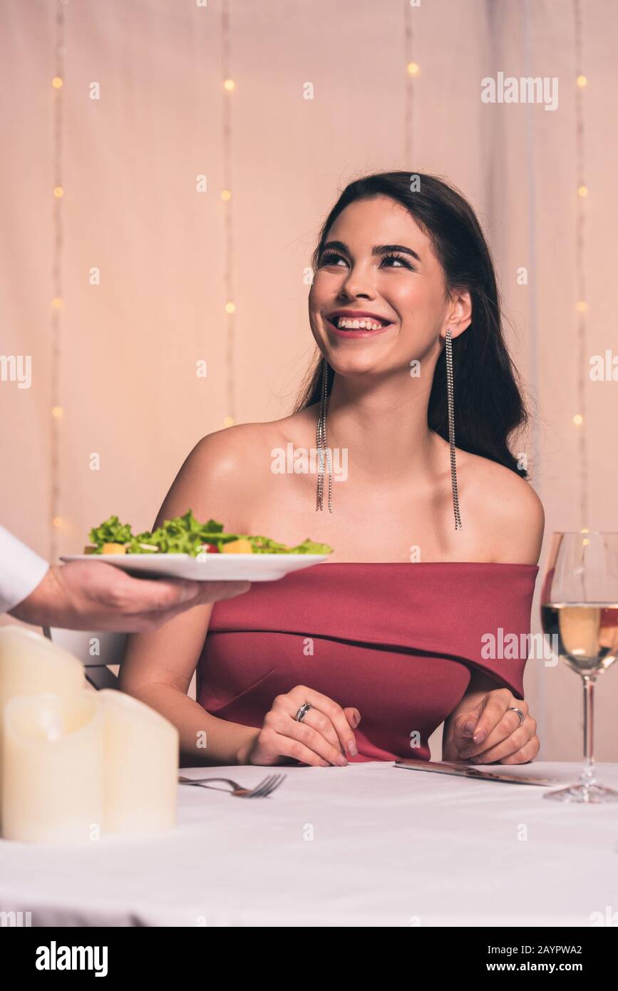 vista dal taglio corto del piatto porta cameriere con insalata fresca vicino a una ragazza allegra ed elegante Foto Stock