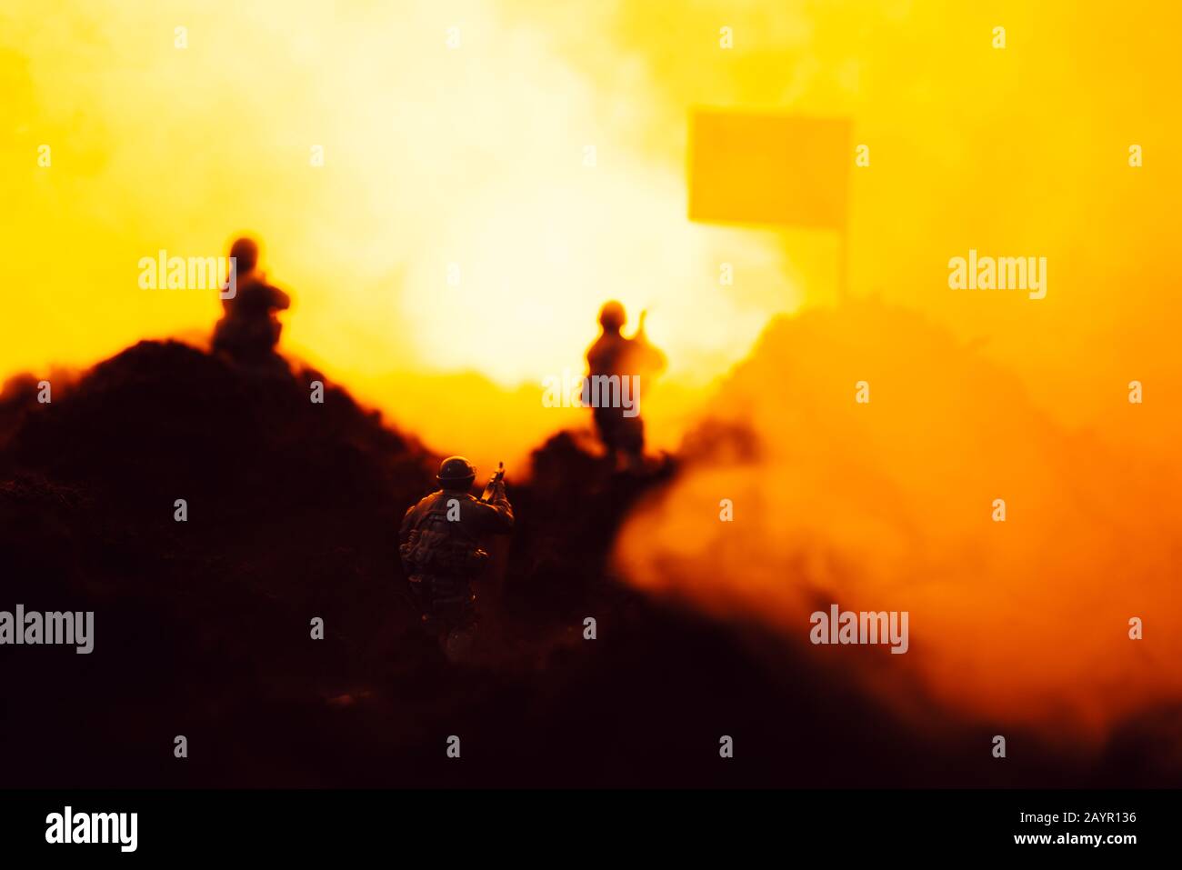 Fuoco selettivo dei guerrieri giocattolo sul campo di battaglia con fumo, bandiera e fuoco sullo sfondo Foto Stock