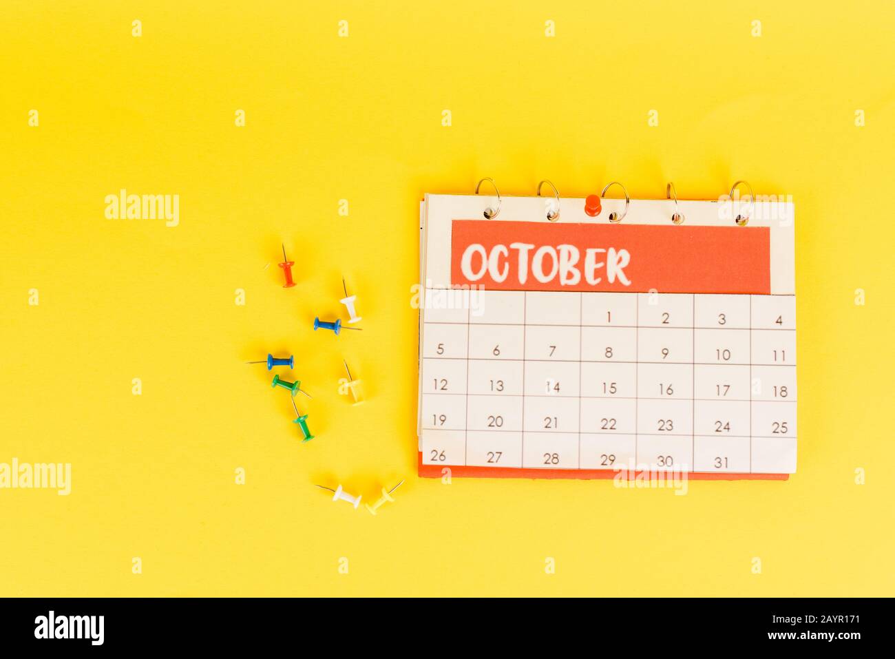 Vista dall'alto del calendario con il mese di ottobre e i PIN dell'ufficio su sfondo giallo Foto Stock