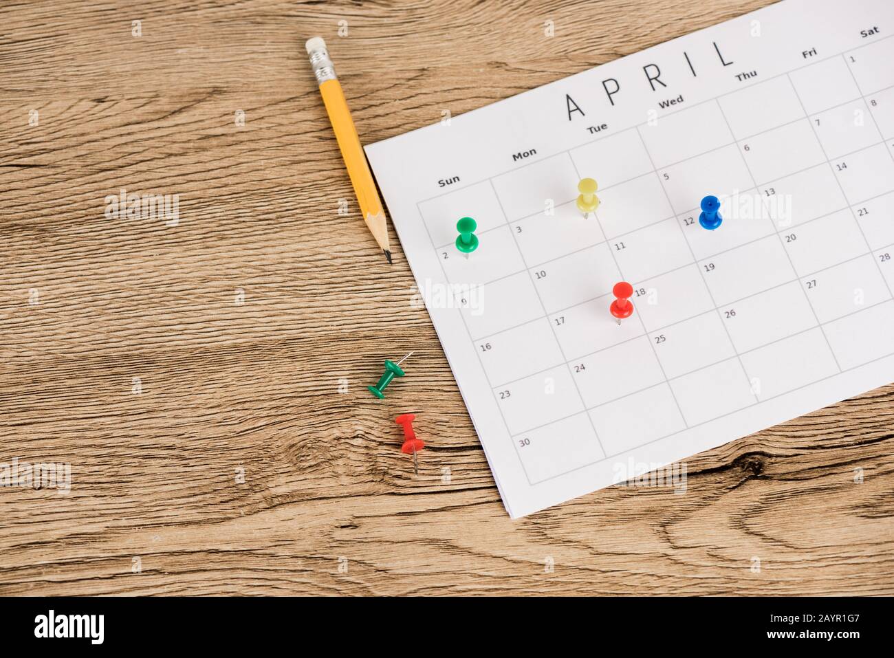 Vista ad alto angolo di matita, spille per ufficio e calendario di aprile su sfondo di legno Foto Stock
