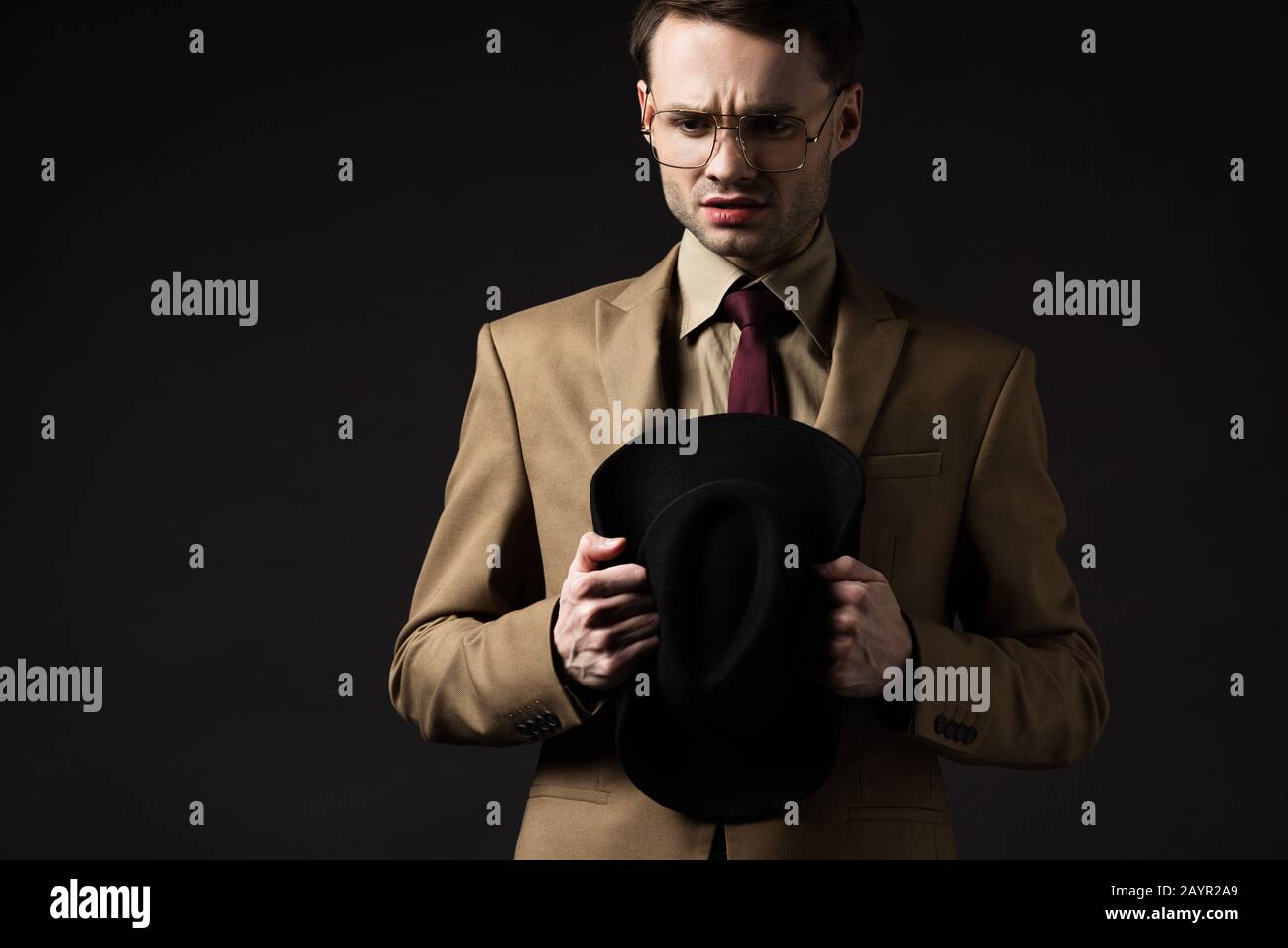 triste uomo elegante in abito beige e occhiali che tengono cappello isolato  su nero Foto stock - Alamy