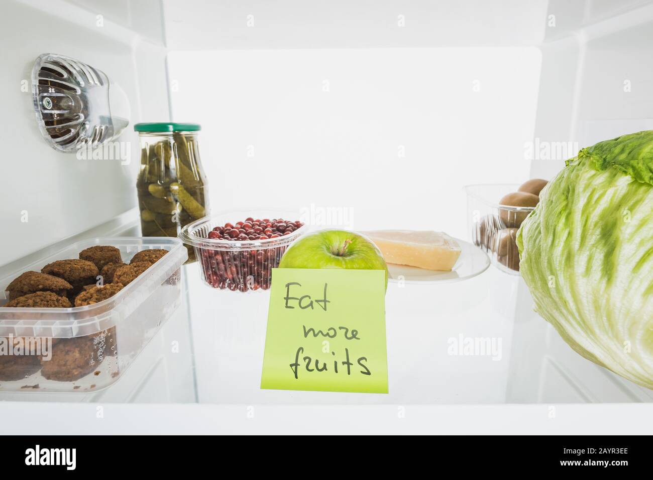 Carta con mangiare più frutta lettering in frigo shelf con cibo isolato su bianco, immagine stock Foto Stock