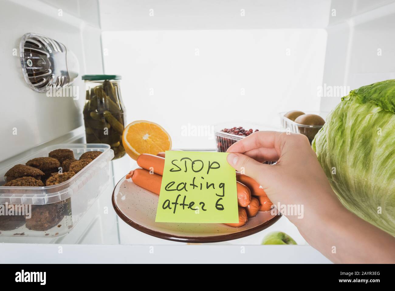 Vista corta della donna con stop mangiare dopo sei lettere su carta con cibo in frigo isolato su bianco, immagine stock Foto Stock