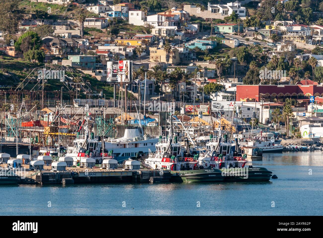 Ensenada, Messico - 17 gennaio 2012: Coca-Cola billboard impostato in città e pescherecci ormeggiato fianco a fianco nel porto. Foto Stock