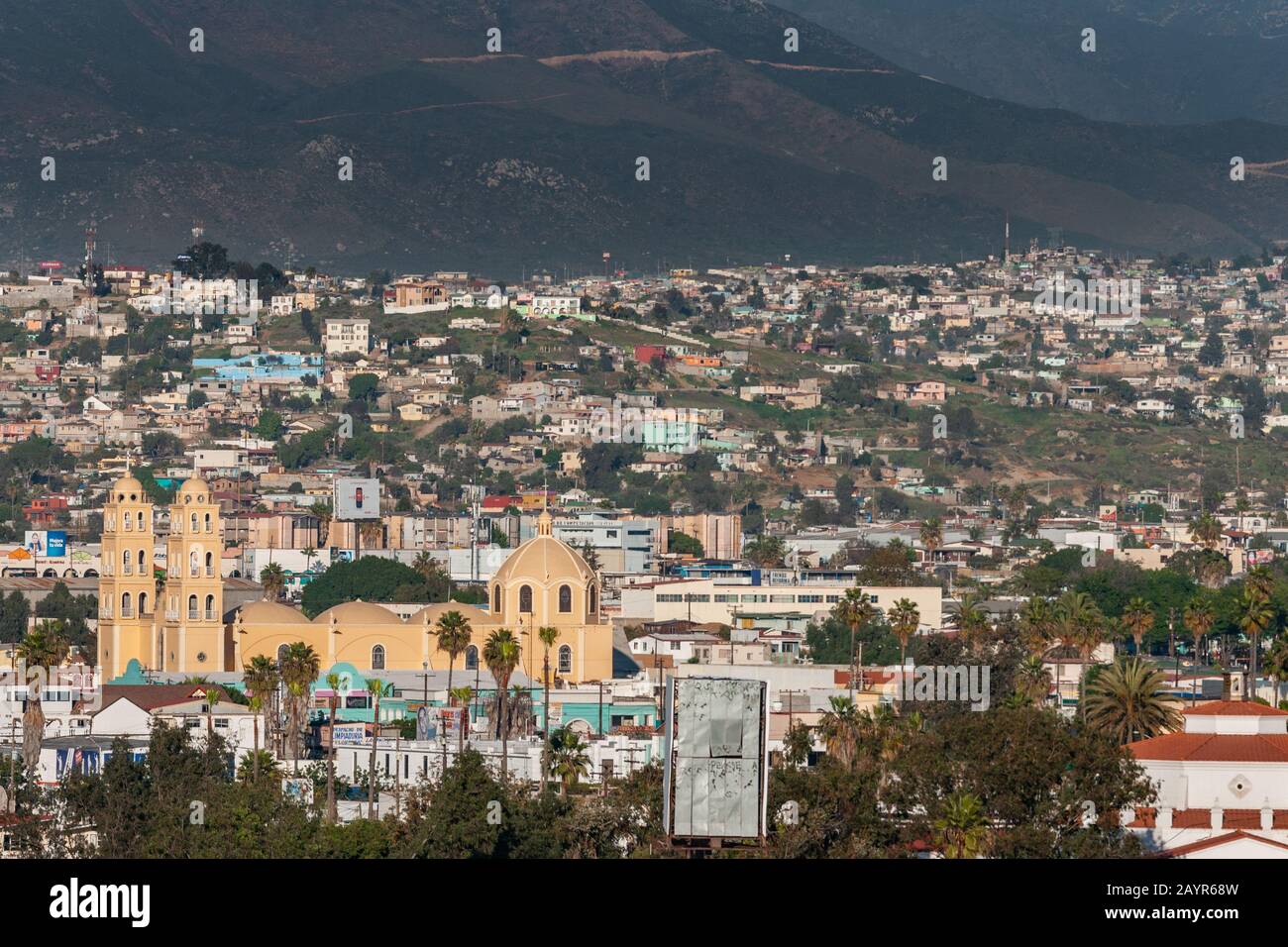 Ensenada, Messico - 17 gennaio 2012: Cattedrale gialla Di Nostra Signora di Guadalupe sotto il sole serale emersed in cityscape e nero pendio di moutain come backd Foto Stock