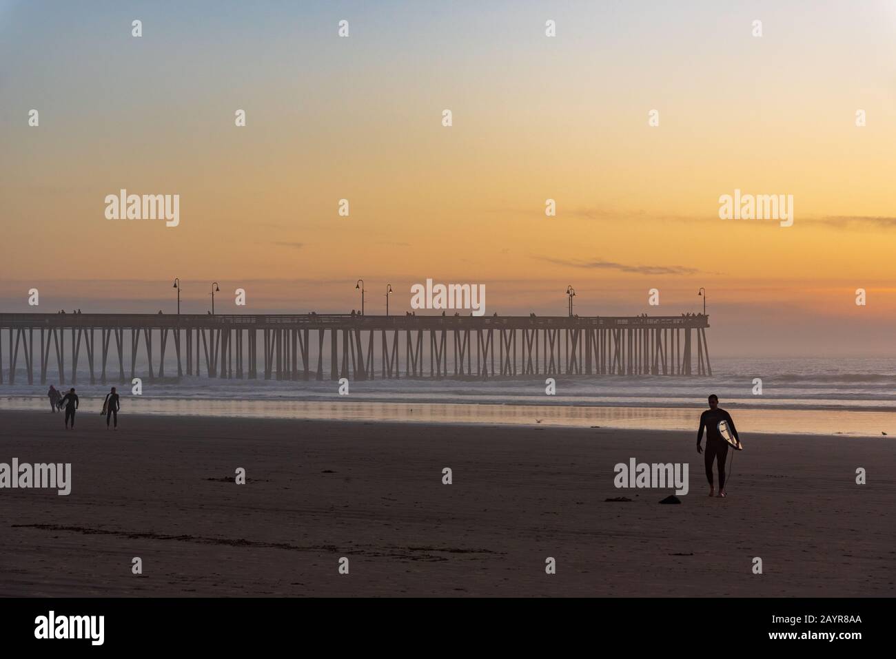 Surfista sulla riva della famosa spiaggia di Pismo in California al tramonto. Foto Stock