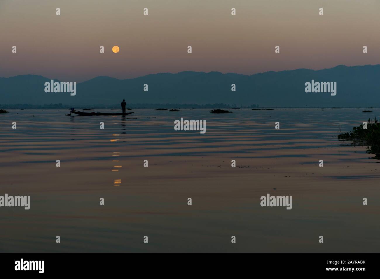 Prima dell'alba sotto una luna piena un pescatore di canottaggio della gamba nella sua barca sta tirando nella sua rete di pesca ha regolato il giorno prima sul lago di Inle in Myanmar. Foto Stock