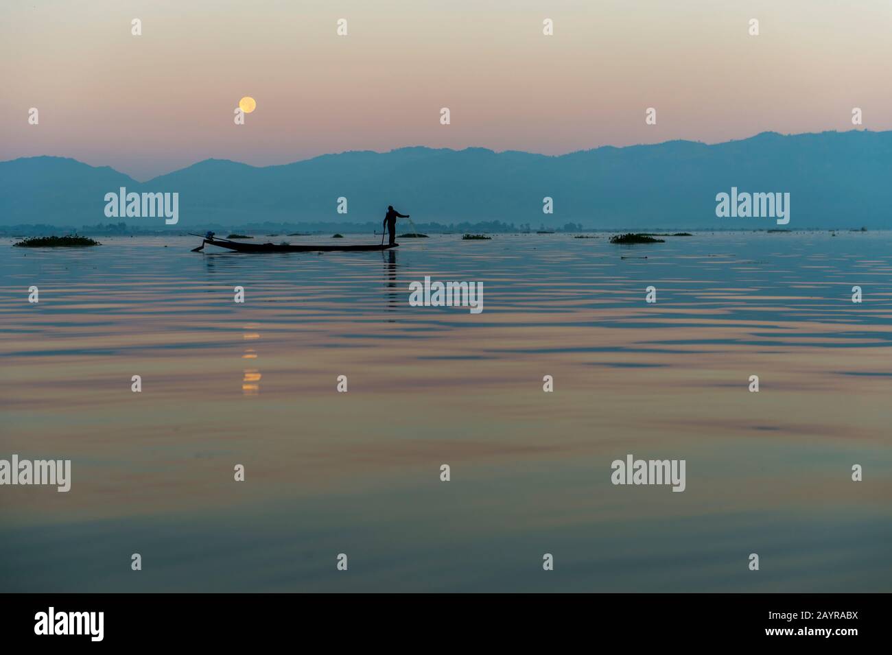 Prima dell'alba sotto una luna piena un pescatore di canottaggio della gamba nella sua barca sta tirando nella sua rete di pesca ha regolato il giorno prima sul lago di Inle in Myanmar. Foto Stock