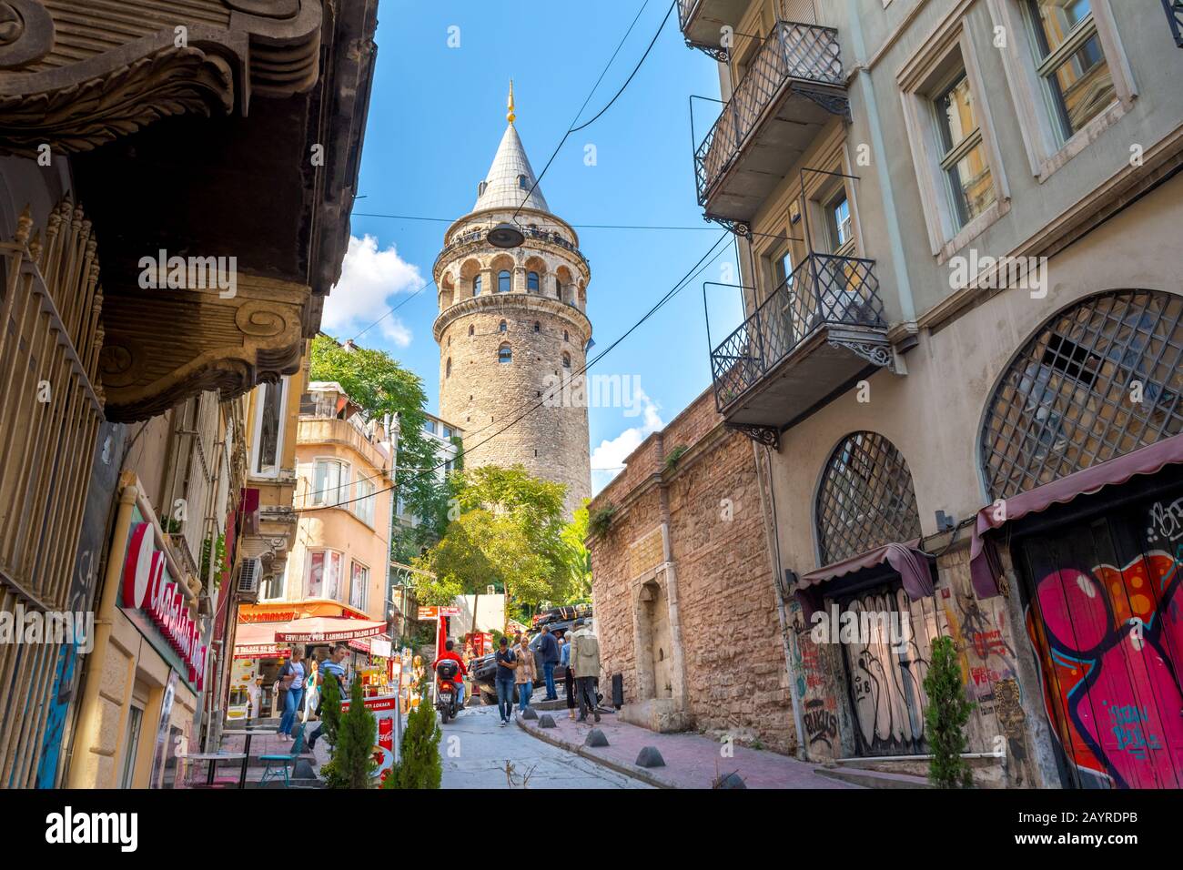 I turisti camminano per le strette strade collinari passando per i negozi sotto la storica Torre Galata nel quartiere Karakoy di Istanbul, Turchia. Foto Stock